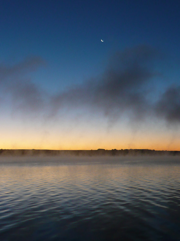 Moon over sunrise on the lake, with lake mist